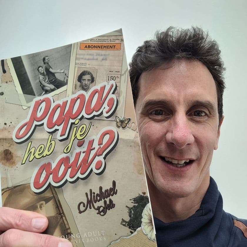Man smiling, holding a book titled "Papa, heb je ooit?" by Michael. The cover features vintage photos and a collage design.