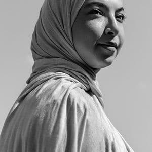 Black and white portrait of a person wearing a headscarf, gazing confidently to the side against a clear sky background.